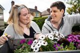 Two women planting white and purple daisies in a wooden trough in the garden at Sandpiper