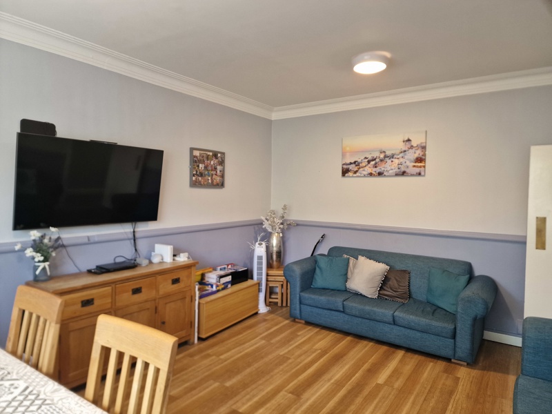 Lounge at Hazeldene with a wall-mounted TV, oak sideboard and blue sofa against lilac-grey walls