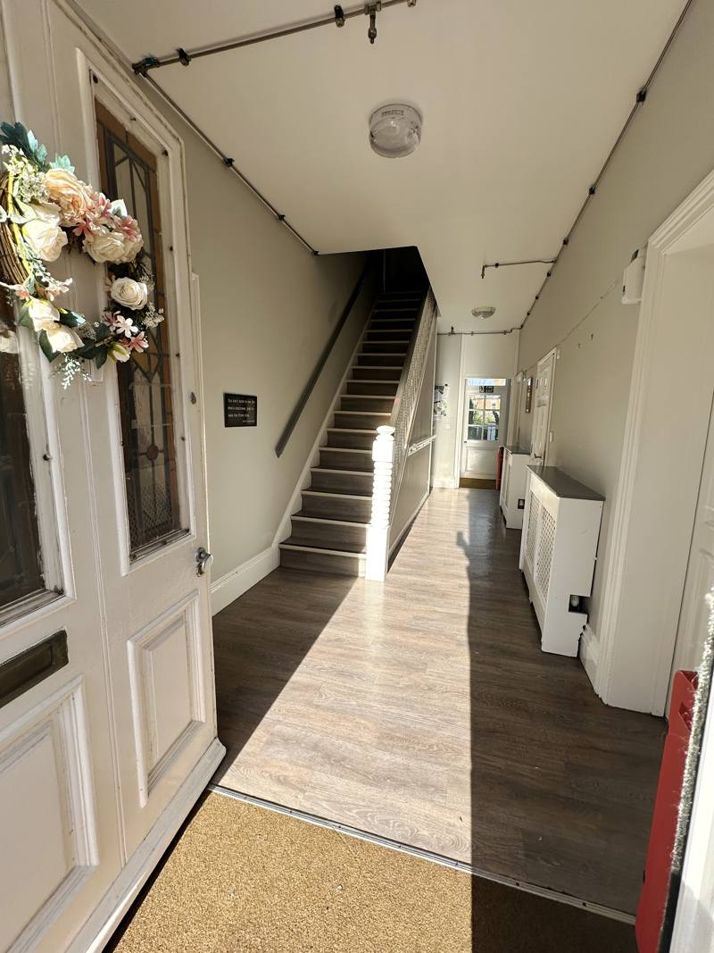 White door with flower decoration leading to light coloured hallway and external door.
