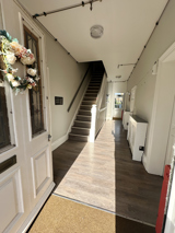 White door with flower decoration leading to light coloured hallway and external door.