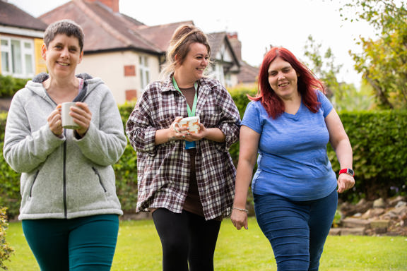 People walking with mugs across the garden lawn at Woburn Sands Lodge with houses behind