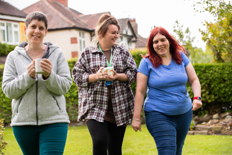 Three women walking and chatting with mugs in the garden in front of the house at Paddocks