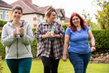 Three women walking and chatting with mugs in the garden in front of the house at Paddocks