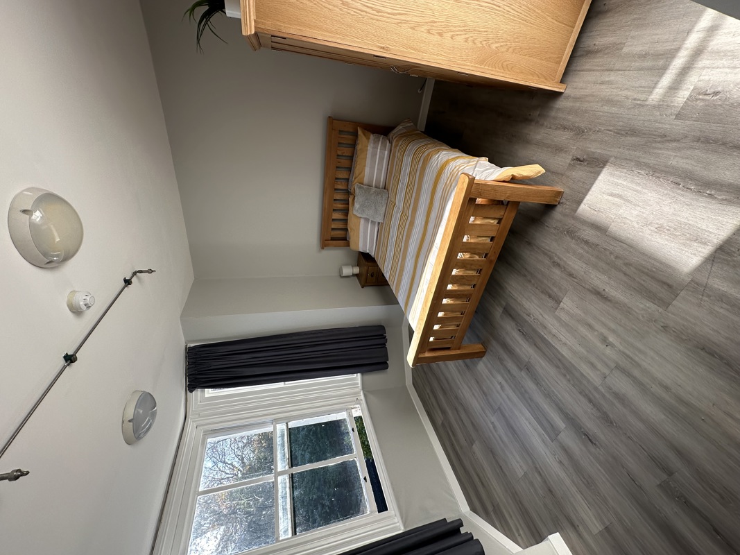 Bedroom at Glanmore with a wooden bed frame, striped bedding, wardrobe and a large sash window
