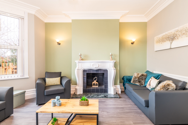 Lounge at Bayview Lodge with grey sofas, a white ornate fireplace and a sage-green feature wall