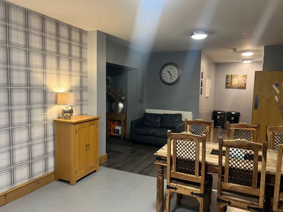 Dining and seating area at Byron Lodge with a wall clock, leather sofa and wooden dining table