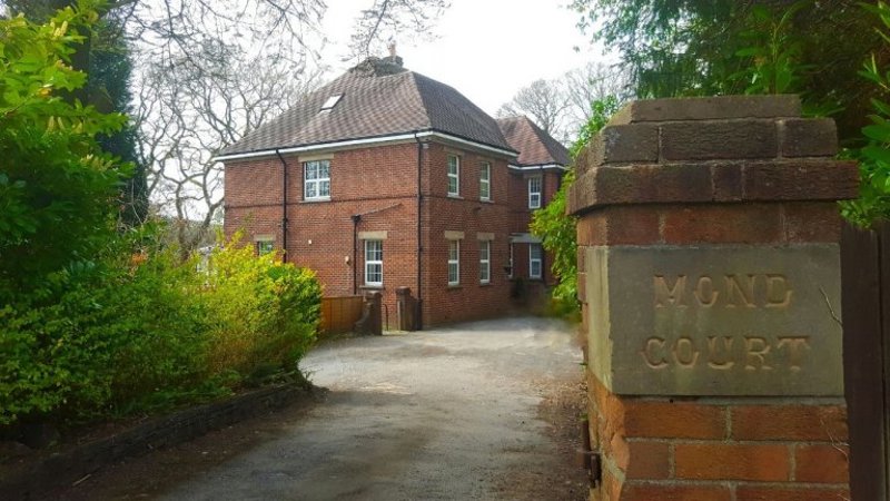 Red-brick exterior of Mond Court Apartments with a driveway and a brick gatepost reading Mond Court