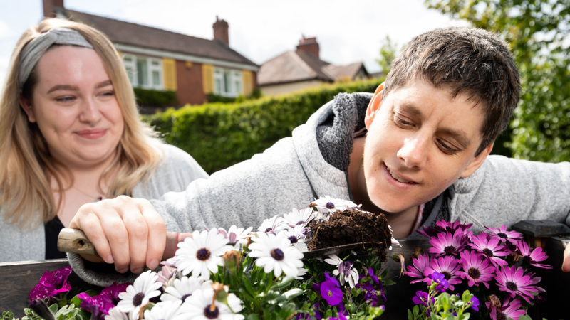 Two people planting white and purple daisies in a garden trough outside the house at The Haven