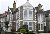 Stone Victorian exterior of Ashcombe Court with white bay windows, gabled roof and a blue name sign
