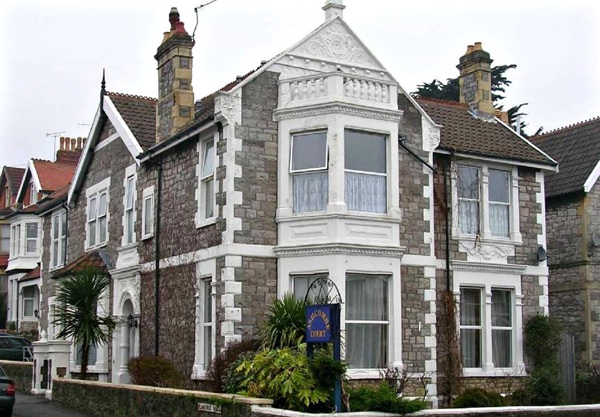 Stone Victorian exterior of Ashcombe Court with white bay windows, gabled roof and a blue name sign
