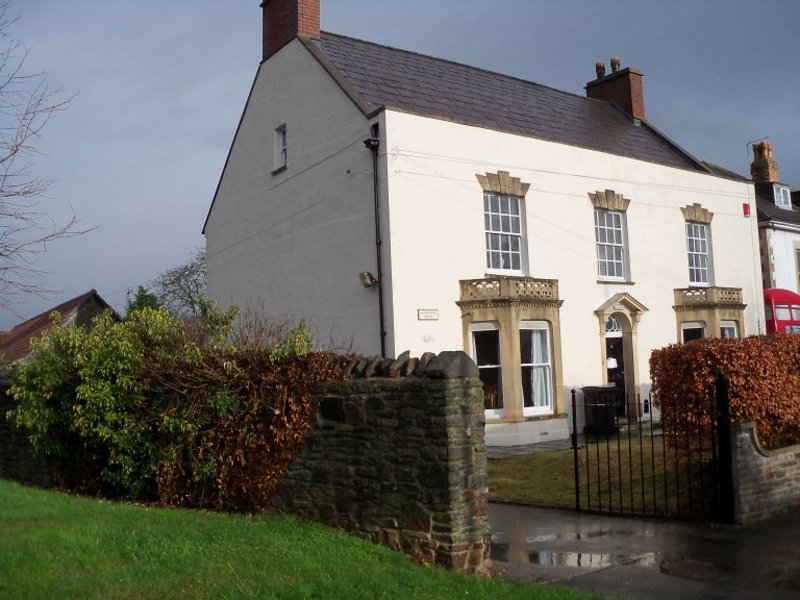 White-rendered period house at Warmley Court with a slate roof, set behind a stone wall and hedge under an overcast sky