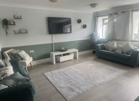 Lounge at Ty Camlas with teal sofas, a wall-mounted TV, a sage green half-wall and a grey rug