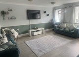 Lounge at Ty Camlas with teal sofas, a wall-mounted TV, a sage green half-wall and a grey rug