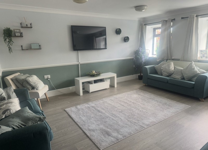 Lounge at Ty Camlas with teal sofas, a wall-mounted TV, a sage green half-wall and a grey rug