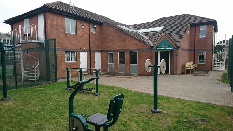 Red-brick exterior and entrance of Park House School with a welcome sign and outdoor gym equipment on the lawn