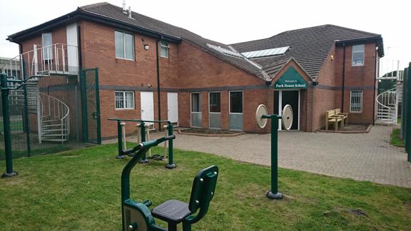 Red-brick exterior and entrance of Park House School with a welcome sign and outdoor gym equipment on the lawn