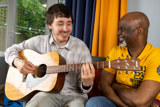 A resident playing acoustic guitar with a support worker in a lounge at Lyndale