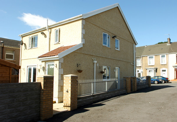 Front exterior of Bakelyn Lodge, a pebbledashed detached house with a tiled porch and a railed brick forecourt