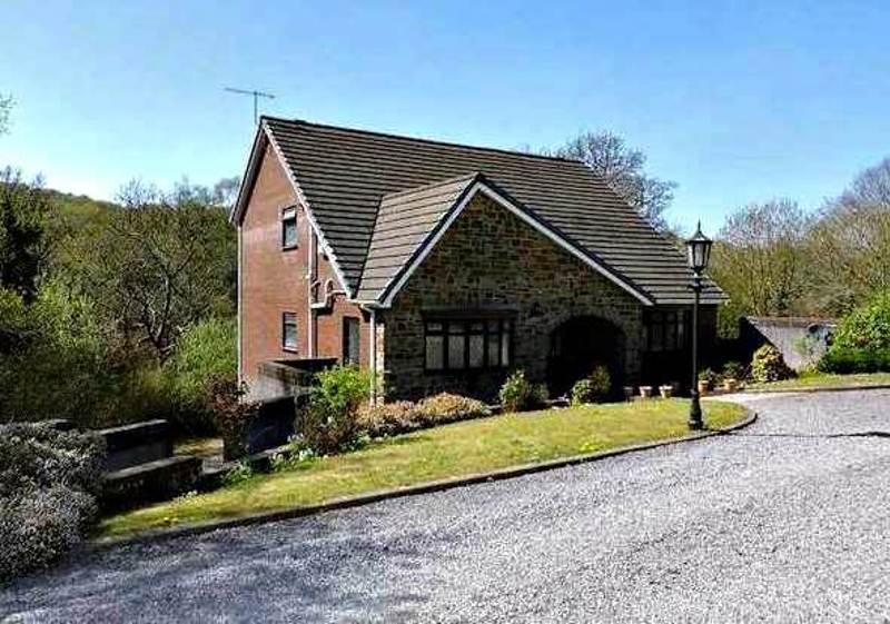Front exterior of Glan Y Felin, a stone and brick detached house with a slate roof and gravel driveway