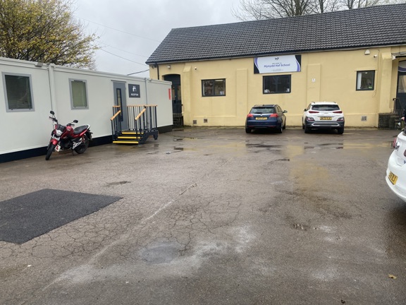 Cream-rendered Mynydd Haf School building with a welcome sign, reception portacabin and cars in the car park