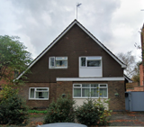 Exterior of St Georges, a detached house with a tile-hung gable, brick lower storey and shrubs by the entrance