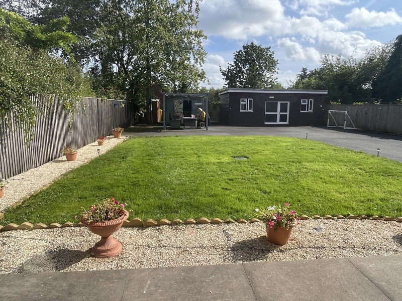 Rear garden at Birchwood House with a lawn, potted flowers and a games room outbuilding