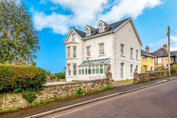 Front exterior of Brynawel, a white Victorian house with bay windows, dormers and a glazed porch by the road