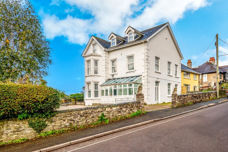 Front exterior of Brynawel, a white Victorian house with bay windows, dormers and a glazed porch by the road