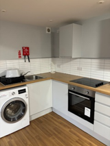 Kitchen at Greenview House with white units, a washing machine, oven, hob and wood-effect flooring