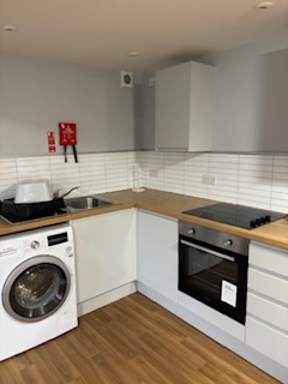 Kitchen at Greenview House with white units, a washing machine, oven, hob and wood-effect flooring