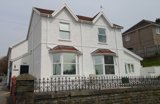 Front exterior of Gwynfryn, a white rendered house with bay windows and ornate iron railings on a stone wall
