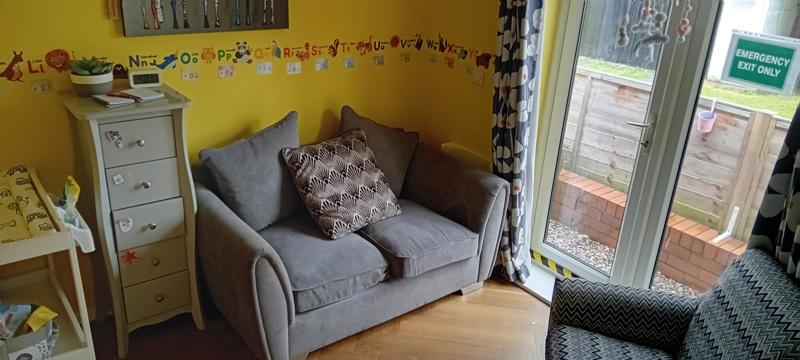 Nursery lounge at Clairmont with a grey sofa, alphabet wall border and patio doors to the garden