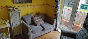 Nursery lounge at Clairmont with a grey sofa, alphabet wall border and patio doors to the garden