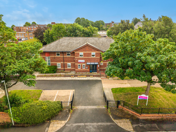 Raised aerial view of the from of a red brick school, with driveway and trees.