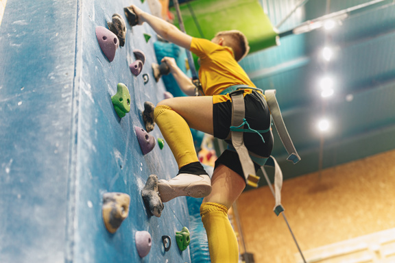 Young person climbing an indoor bouldering wall in a harness and yellow kit at Keys Alternative Learning