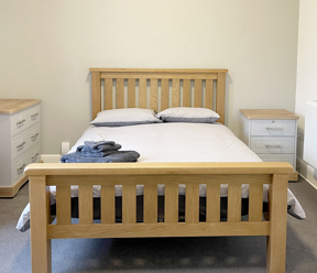 Light coloured wooden bed with grey duvet and 2 bedside drawers