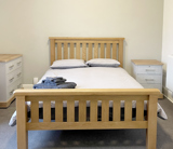 Light coloured wooden bed with grey duvet and 2 bedside drawers