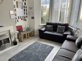 Lounge at Thompson Court with brown leather sofas, a fireplace, grey rug and a photo display wall