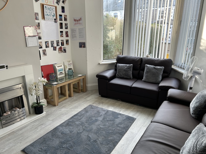 Lounge at Thompson Court with brown leather sofas, a fireplace, grey rug and a photo display wall