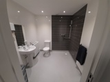 Accessible wet room at Boston House with a walk-in shower, toilet, basin and grey feature tiling