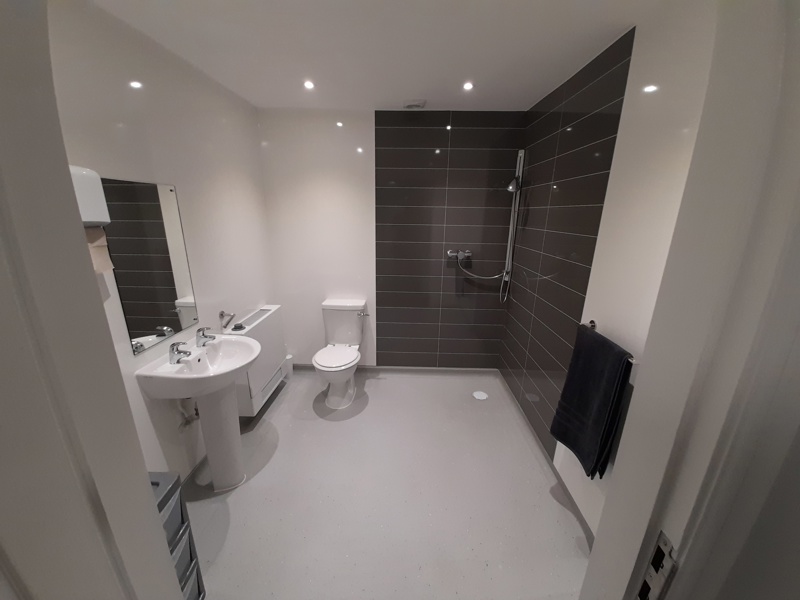 Accessible wet room at Boston House with a walk-in shower, toilet, basin and grey feature tiling