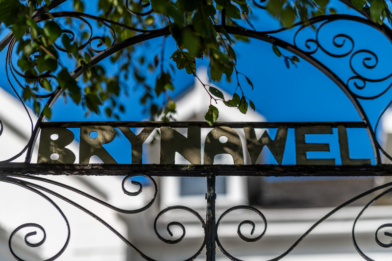 Wrought-iron gate at Brynawel with brass lettering spelling the home's name and a white facade behind