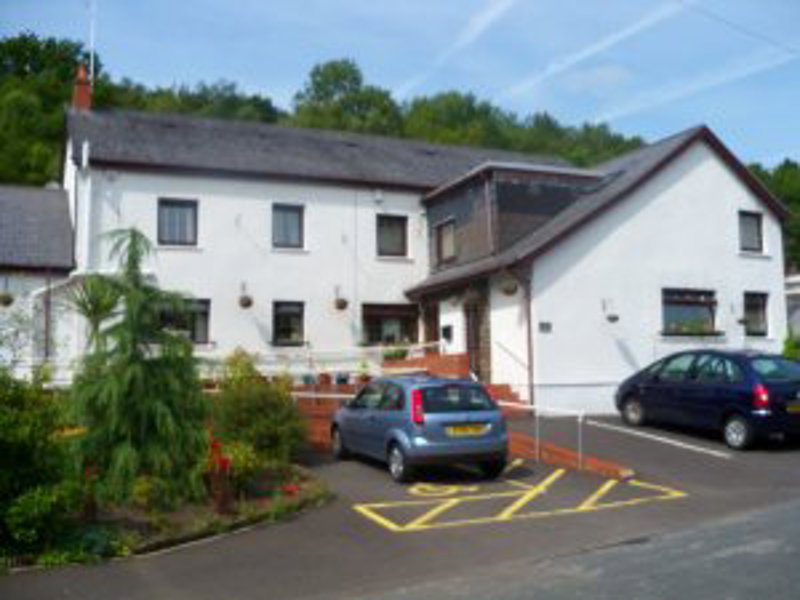 Exterior of Ty Camlas, a white two-storey care home with cars parked in front and hedged borders