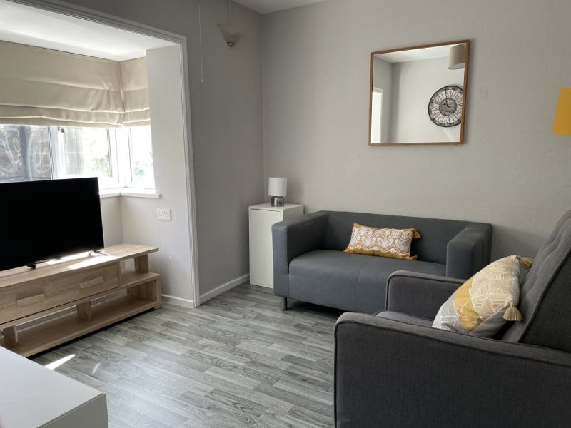 Back lounge at Princes Court with grey sofas, mustard cushions, a wall mirror and a TV on a wooden stand