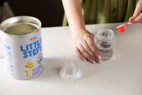 Hands measuring a scoop of infant formula into a bottle at Crown House family assessment centre