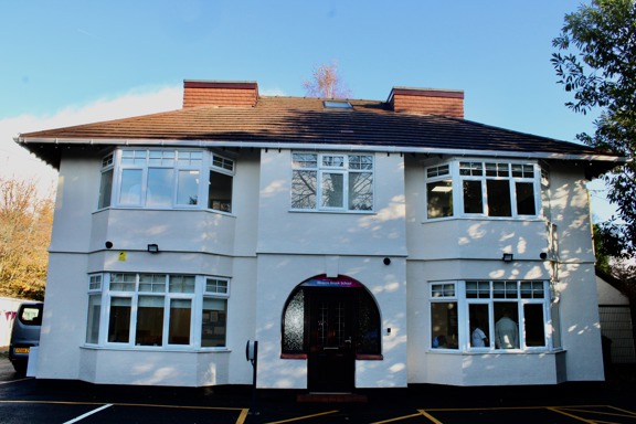 White rendered front of Rivacre Brook School with bay windows and an arched entrance under a blue sky