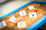 Reading cards with images stuck into golden sand in a light blue table-top sand pit
