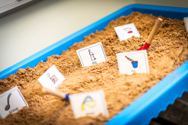 Reading cards with images stuck into golden sand in a light blue table-top sand pit