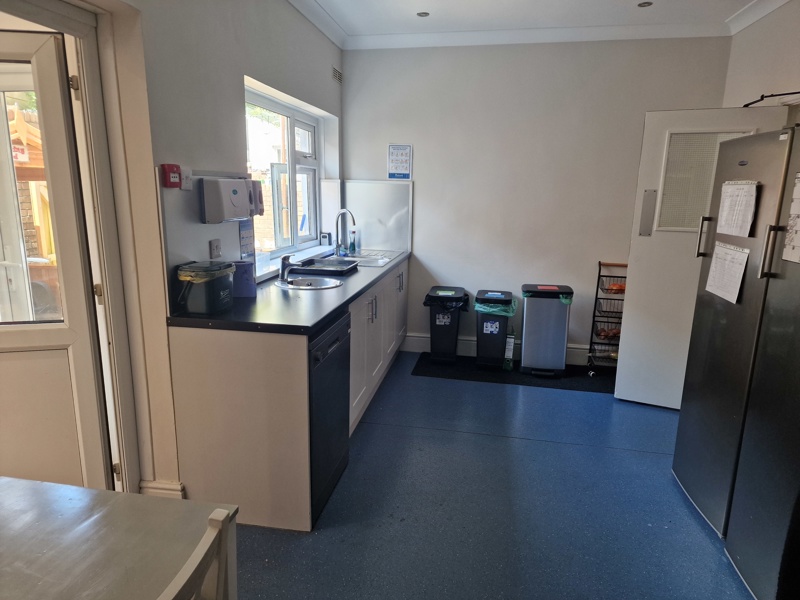 Kitchen at Hazeldene with white units, black worktop, a sink under the window and recycling bins