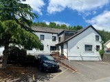 Exterior of Ty Camlas, a white-rendered care home with a slate roof, parking area and wooded hillside behind